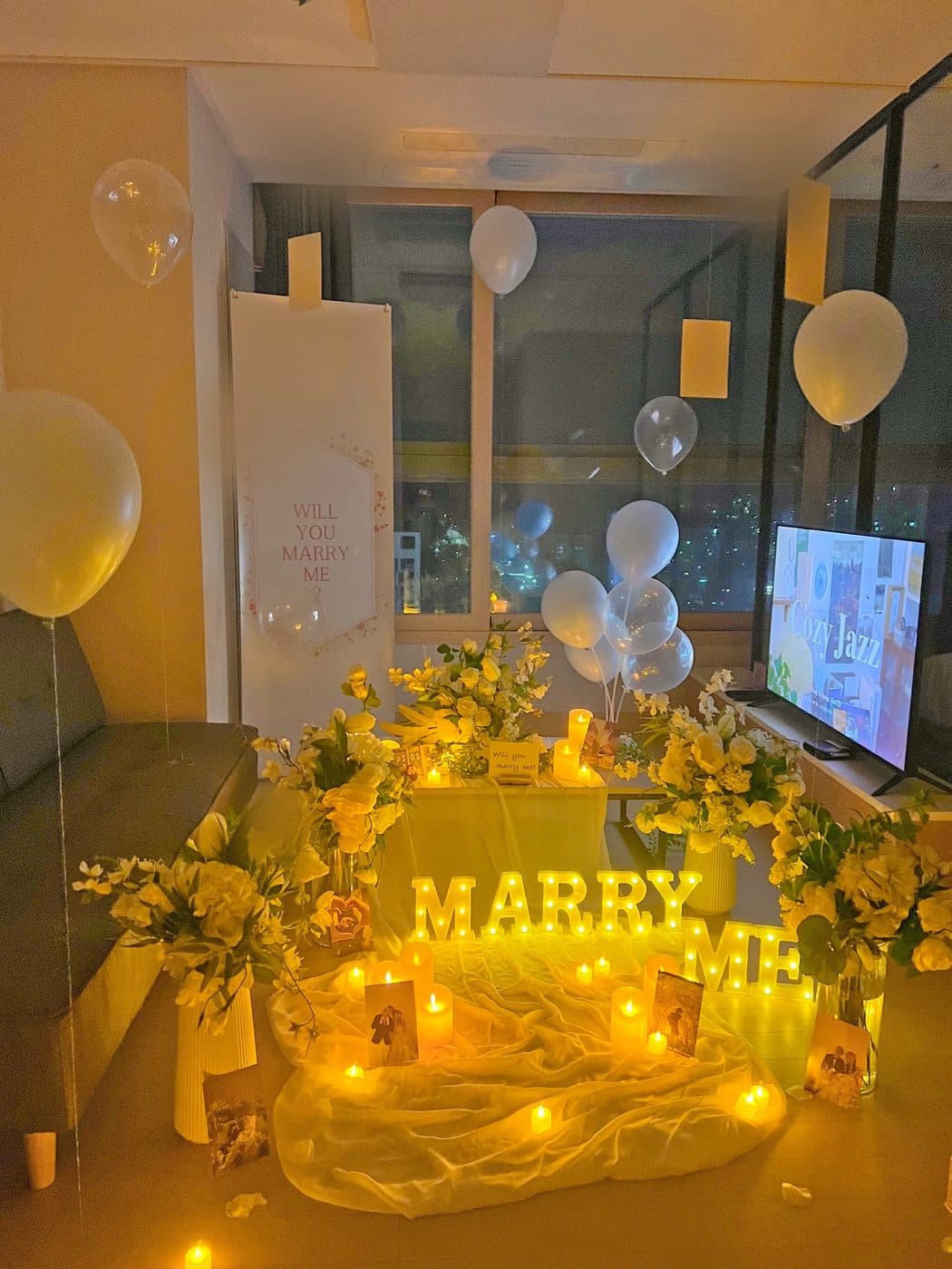자택 거실에 노란 꽃다발 네 개를 놓고 MARRY ME 조명을 켠 뒤 사진을 세워둔 저녁 프로포즈 현장